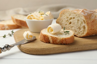 Photo of Cut baguette with butter and herbs on white wooden table, closeup