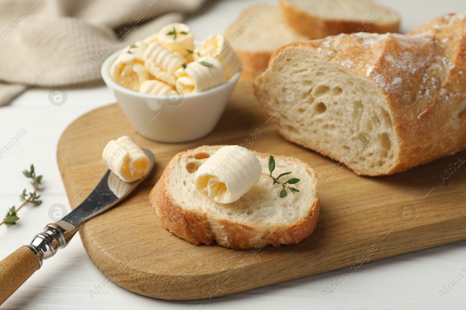 Photo of Cut baguette with butter and herbs on white wooden table, closeup