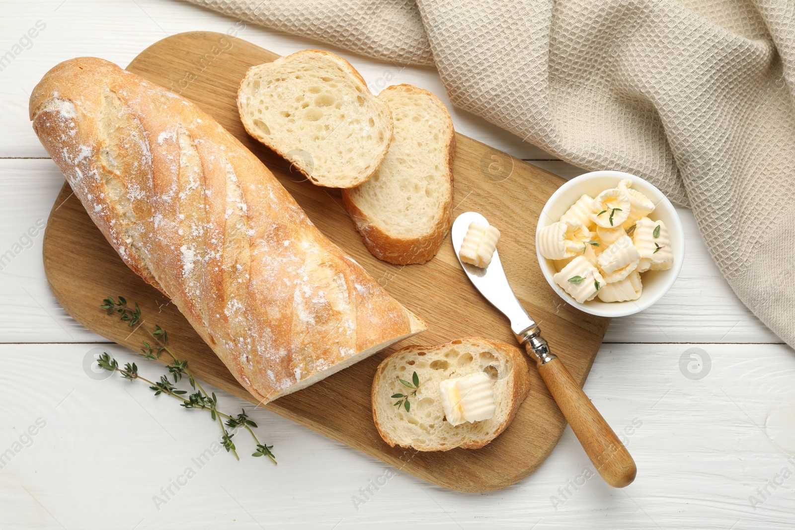 Photo of Cut baguette with butter and herbs on white wooden table, flat lay