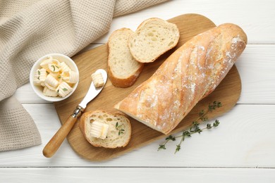 Photo of Cut baguette with butter and herbs on white wooden table, flat lay