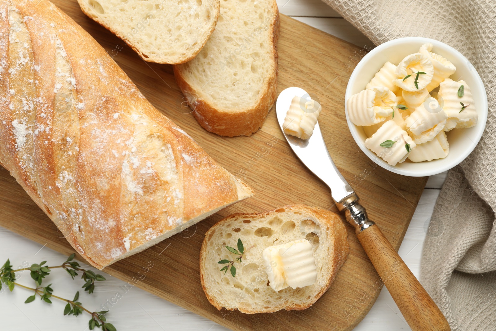 Photo of Cut baguette with butter and herbs on white wooden table, flat lay