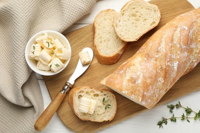 Photo of Cut baguette with butter and herbs on white wooden table, flat lay