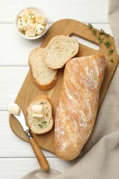 Photo of Cut baguette with butter and herbs on white wooden table, flat lay