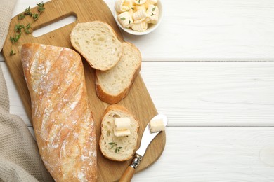 Photo of Cut baguette with butter and herbs on white wooden table, flat lay. Space for text