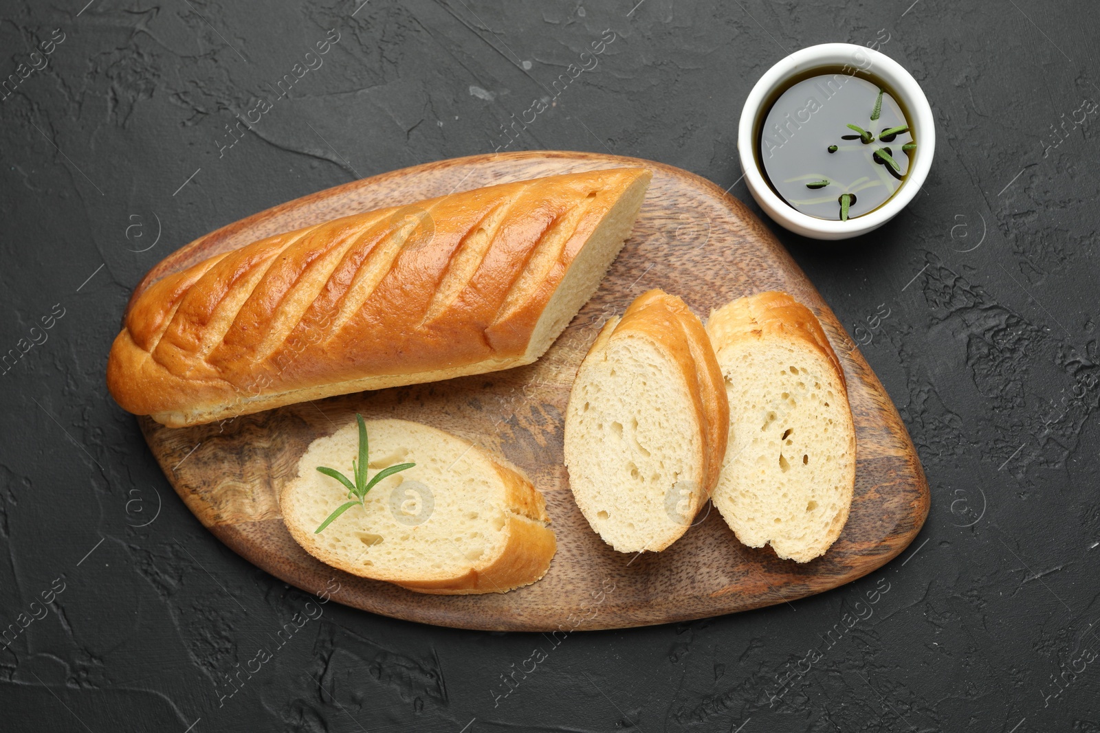 Photo of Cut fresh baguette with balsamic and rosemary on black table, top view