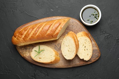 Photo of Cut fresh baguette with balsamic and rosemary on black table, top view