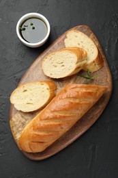 Photo of Cut fresh baguette with balsamic and rosemary on black table, top view