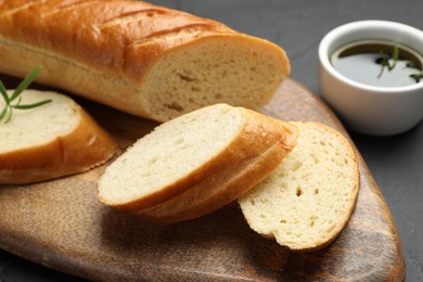 Photo of Cut fresh baguette with balsamic and rosemary on black table, closeup