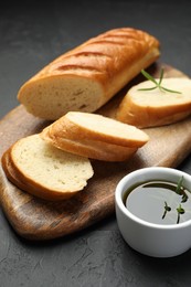 Photo of Cut fresh baguette with balsamic and rosemary on black table, closeup