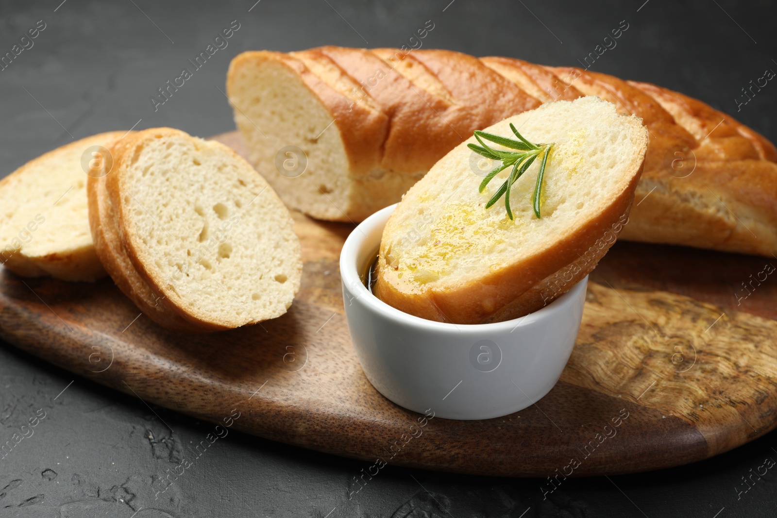 Photo of Cut fresh baguette with balsamic and rosemary on black table, closeup