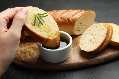 Photo of Woman dipping slice of tasty baguette into balsamic at black table, closeup