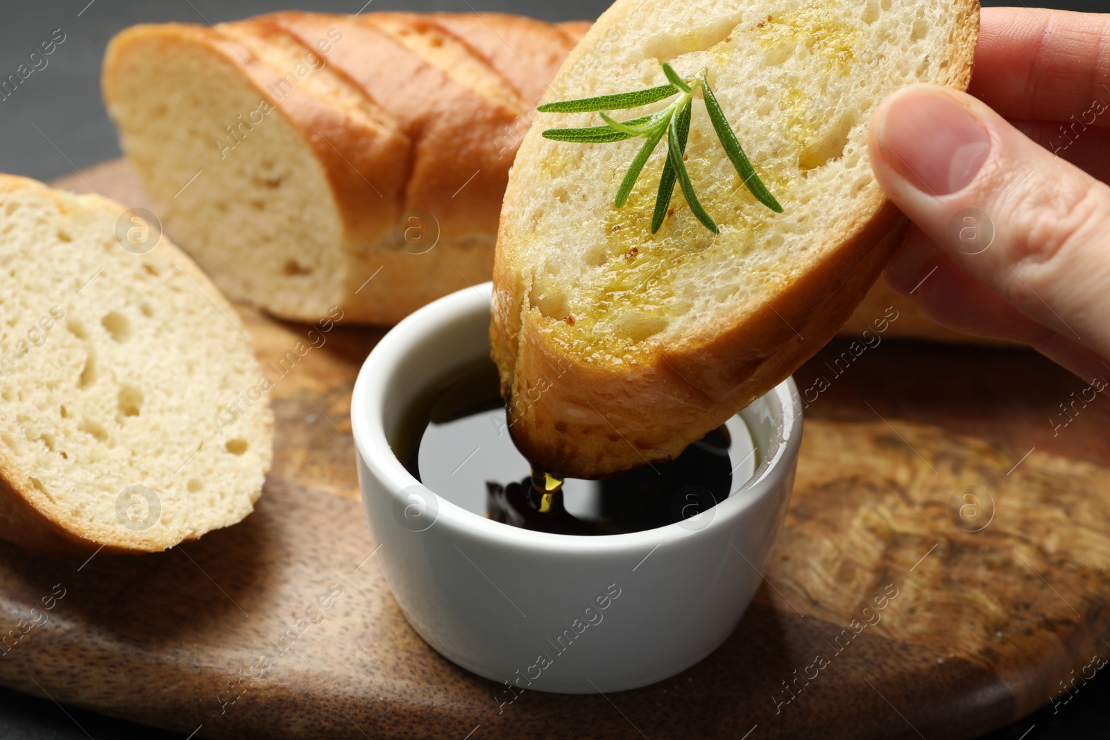 Photo of Woman dipping slice of tasty baguette into balsamic at table, closeup