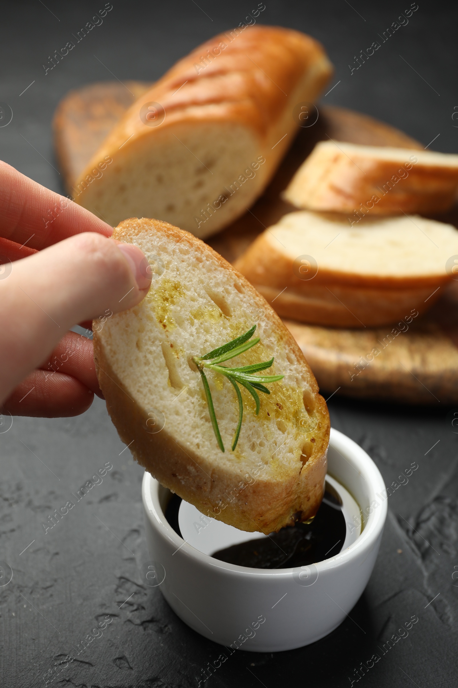 Photo of Woman dipping slice of tasty baguette into balsamic at black table, closeup