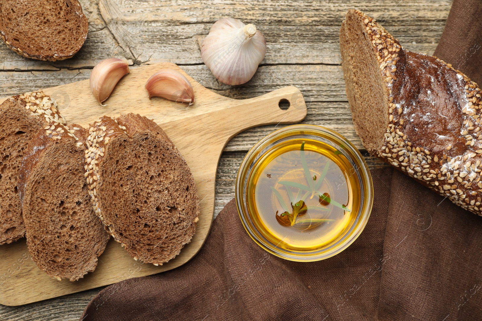 Photo of Slices of rye baguette, oil and garlic on wooden table, flat lay