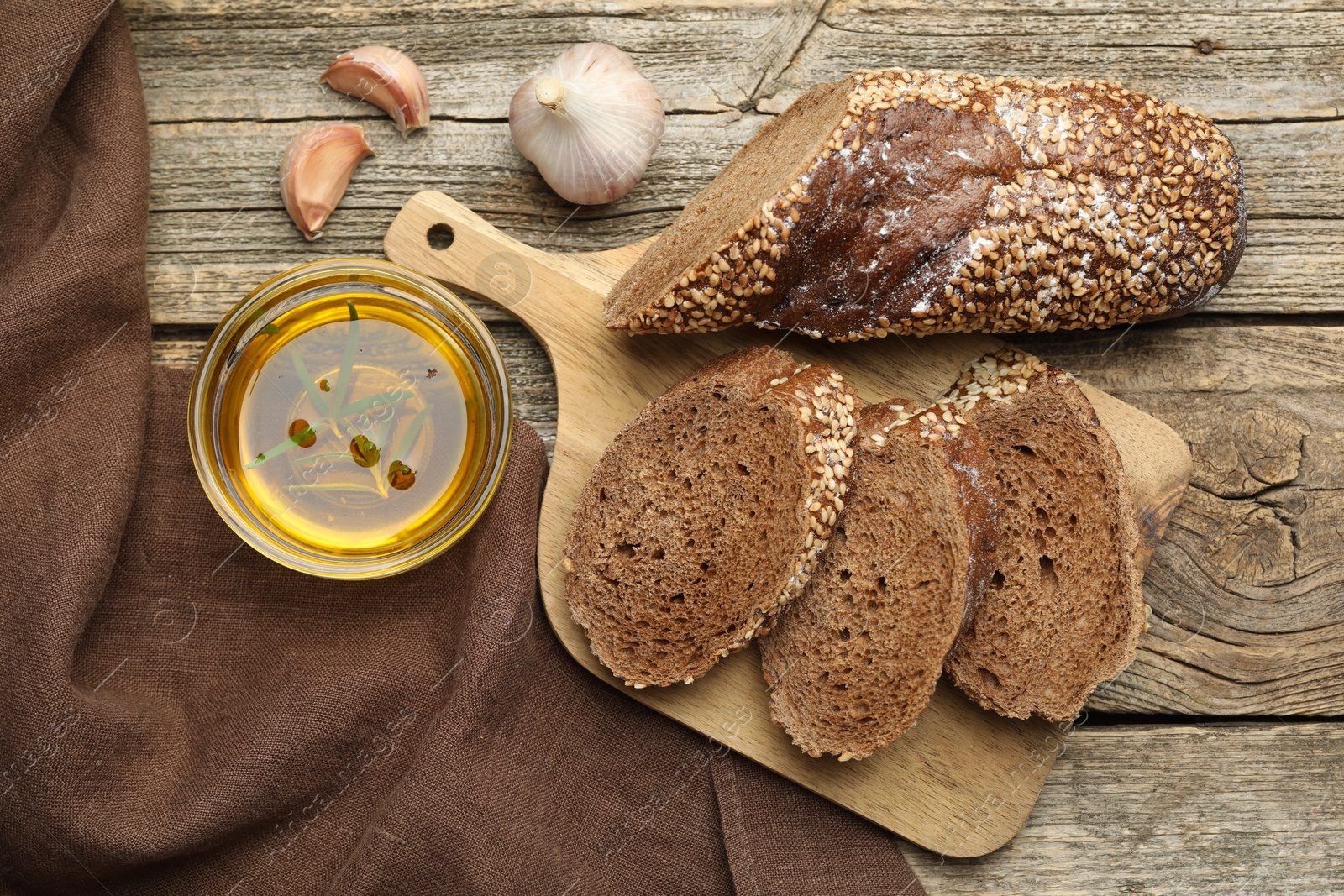 Photo of Slices of rye baguette, oil and garlic on wooden table, flat lay