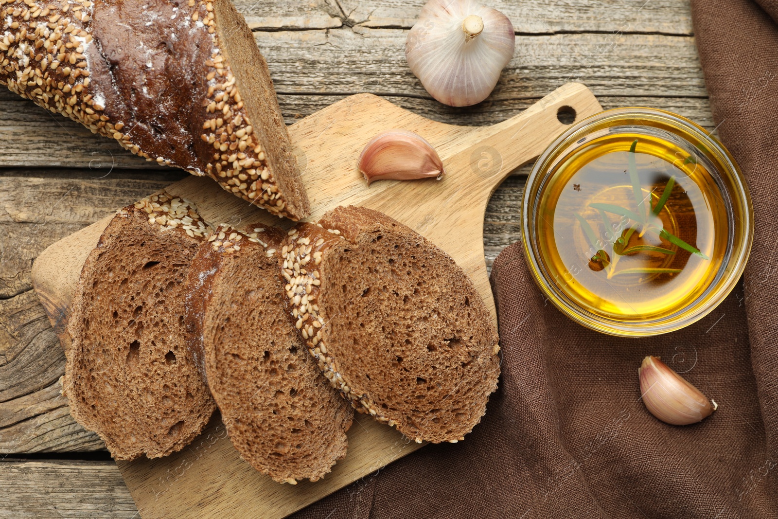 Photo of Slices of rye baguette, oil and garlic on wooden table, flat lay