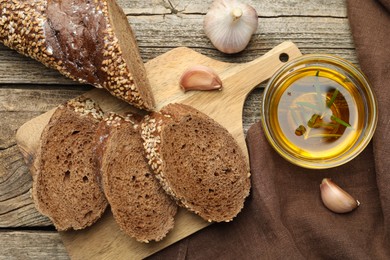 Photo of Slices of rye baguette, oil and garlic on wooden table, flat lay