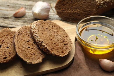 Photo of Slices of rye baguette, oil and garlic on wooden table, closeup