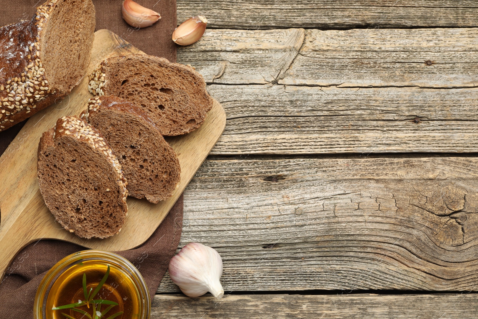 Photo of Slices of rye baguette, oil and garlic on wooden table, flat lay. Space for text