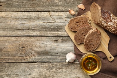 Photo of Slices of rye baguette, oil and garlic on wooden table, flat lay. Space for text