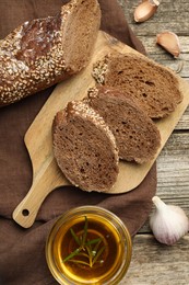 Photo of Slices of rye baguette, oil and garlic on wooden table, flat lay