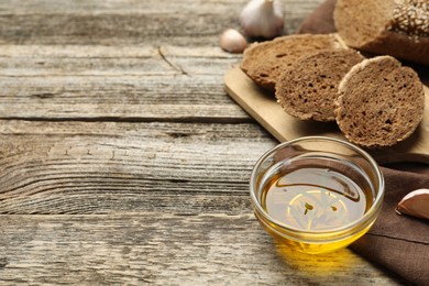 Photo of Slices of rye baguette, oil and garlic on wooden table, closeup. Space for text