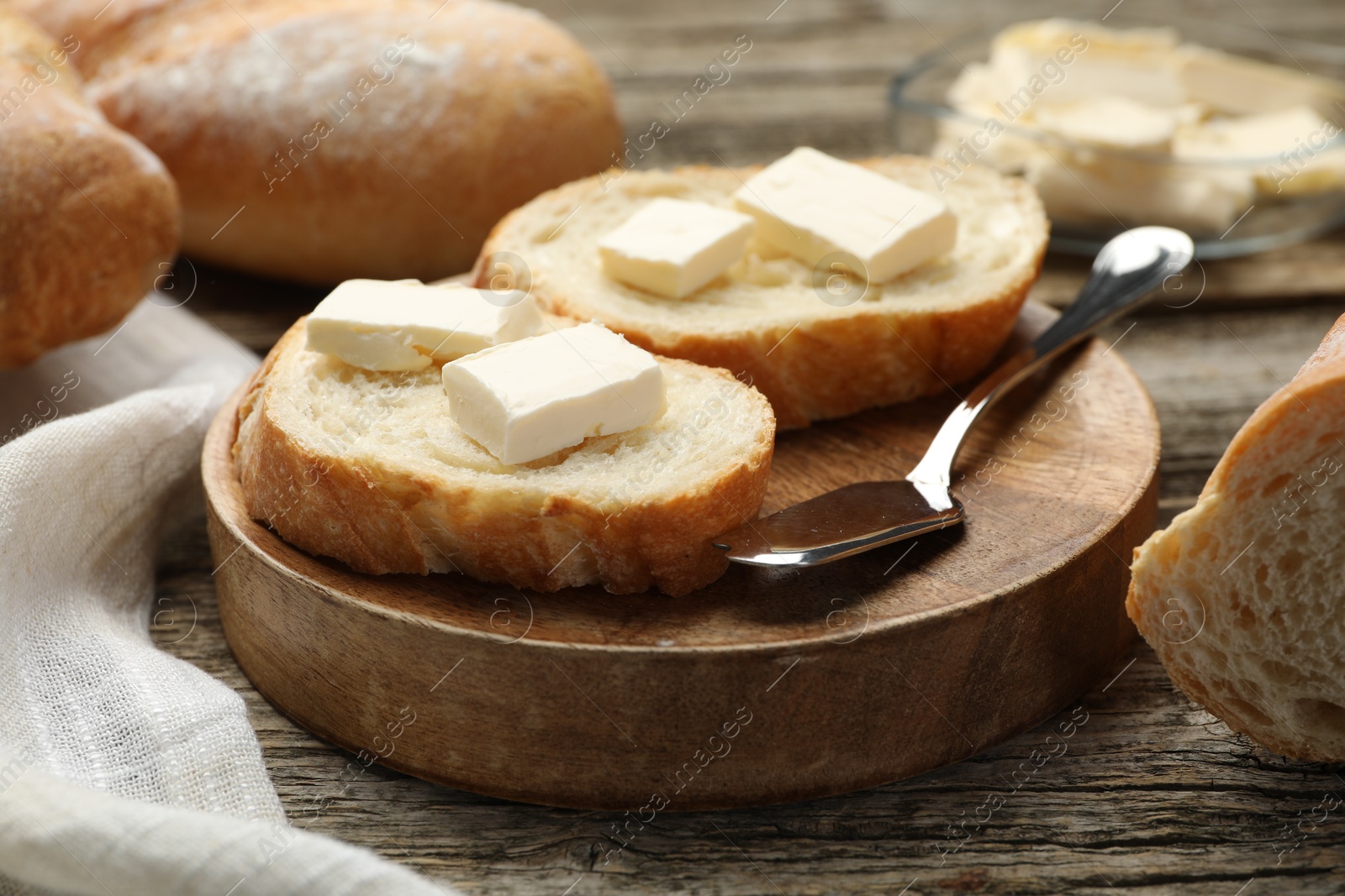 Photo of Slices of fresh baguette with butter on wooden table, closeup