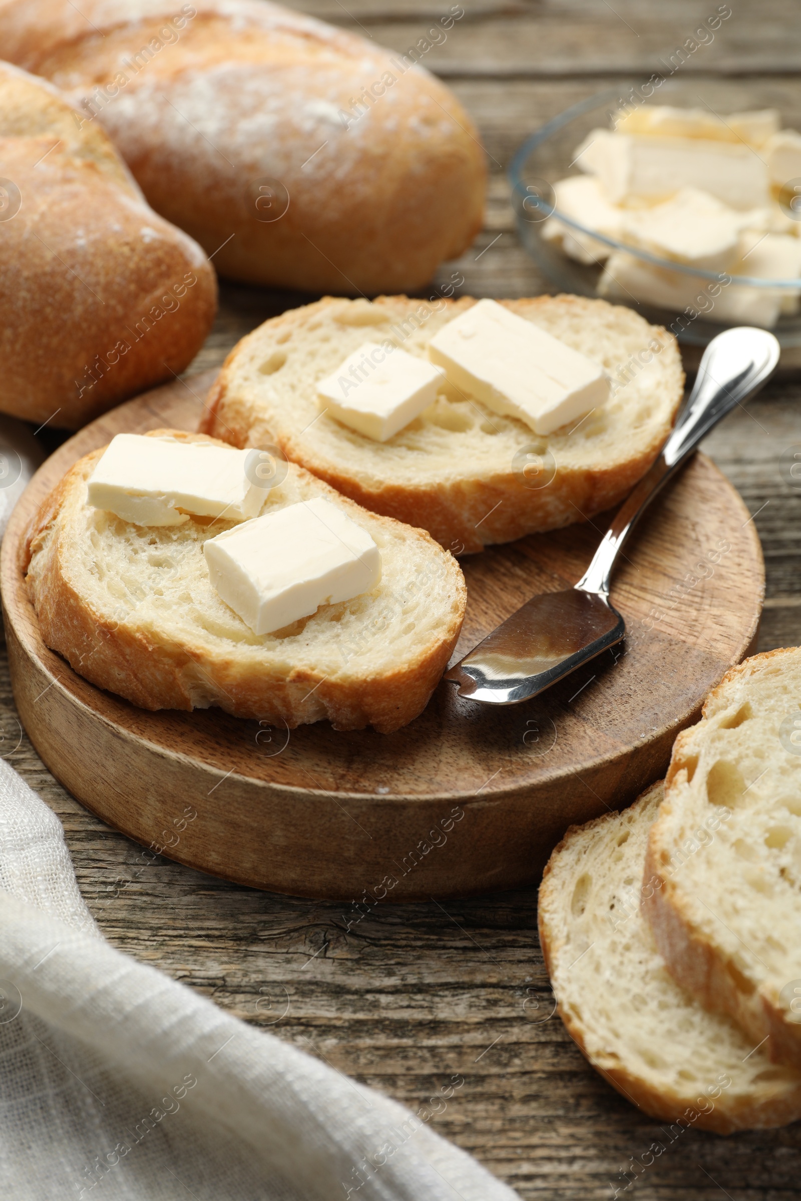 Photo of Slices of fresh baguette with butter on wooden table, closeup