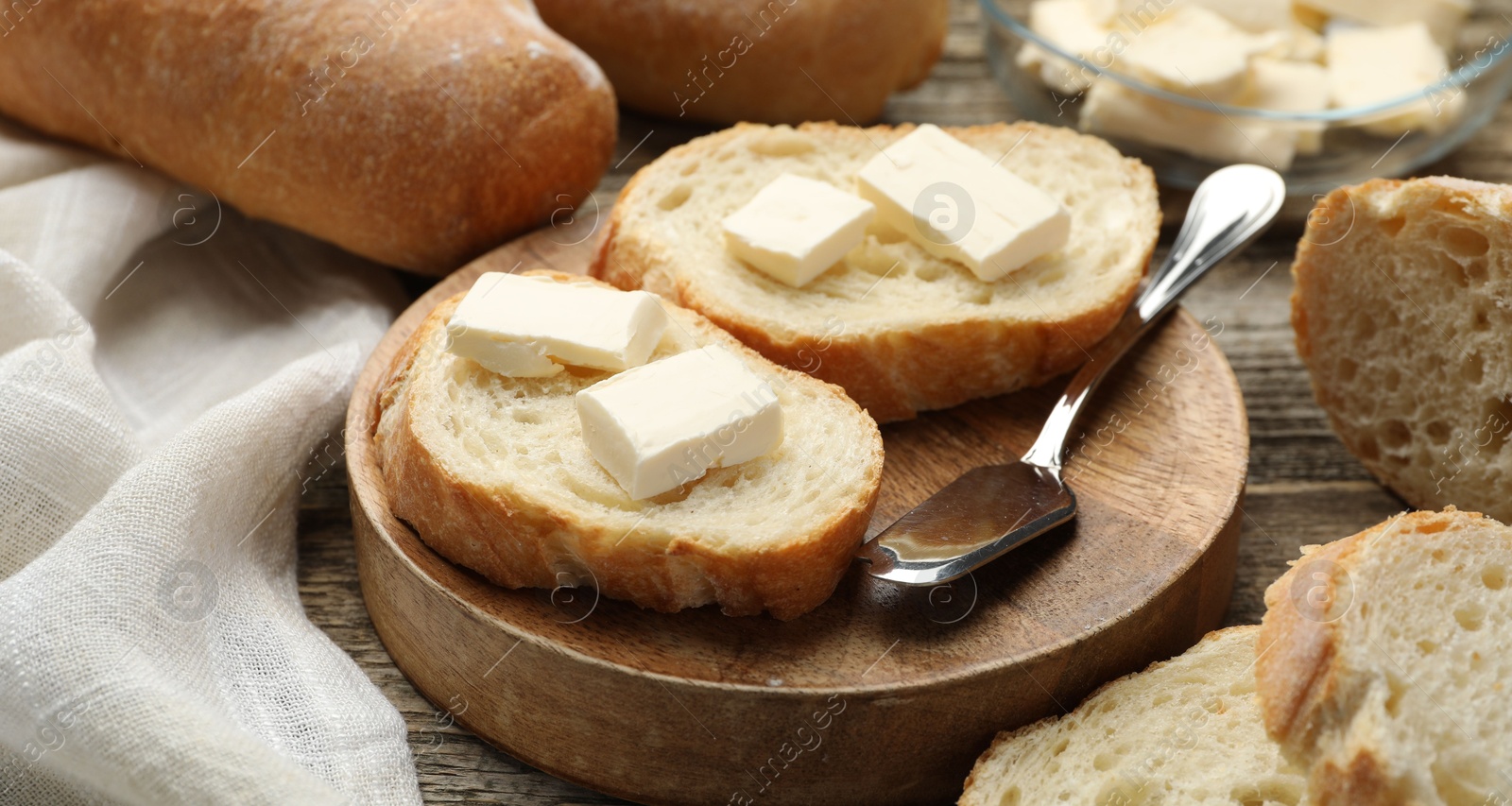 Photo of Slices of fresh baguette with butter on wooden table, closeup