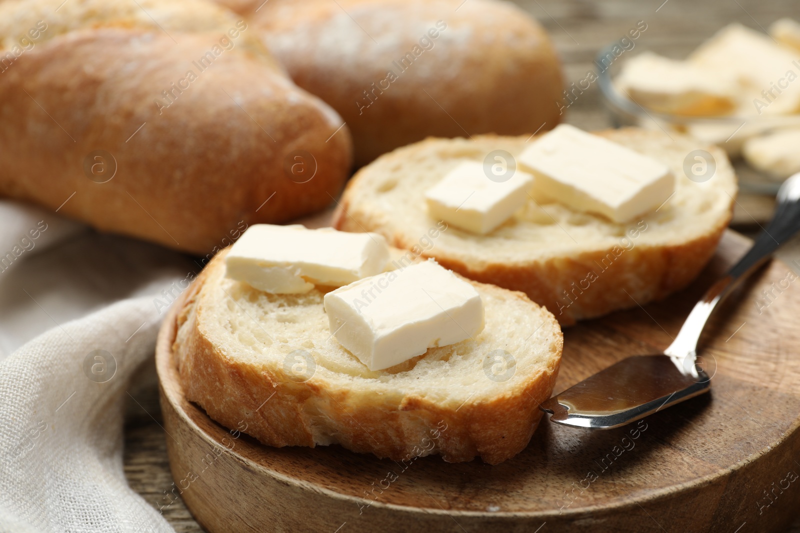 Photo of Slices of fresh baguette with butter on wooden table, closeup