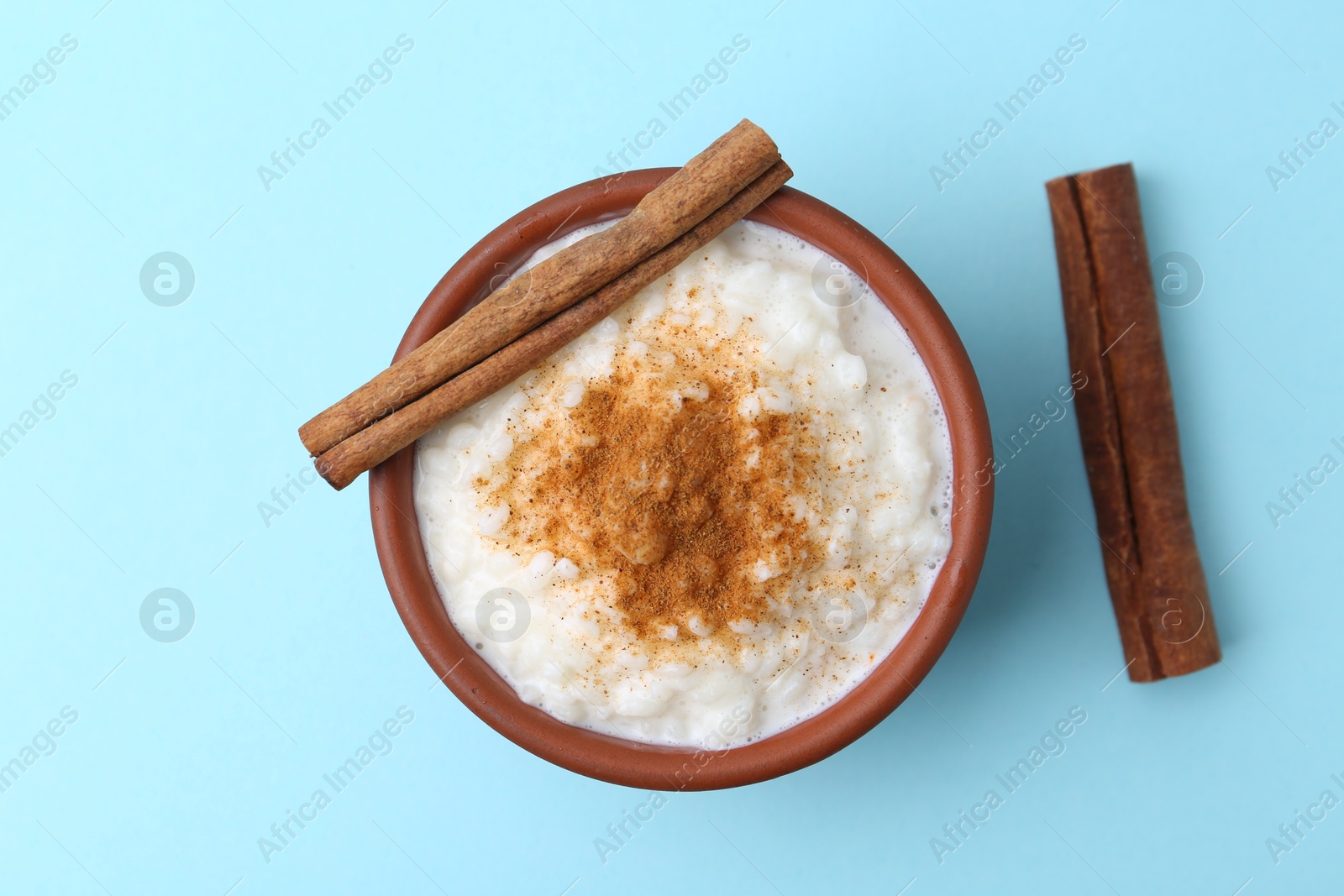 Photo of Delicious rice pudding with cinnamon sticks on light blue background, top view