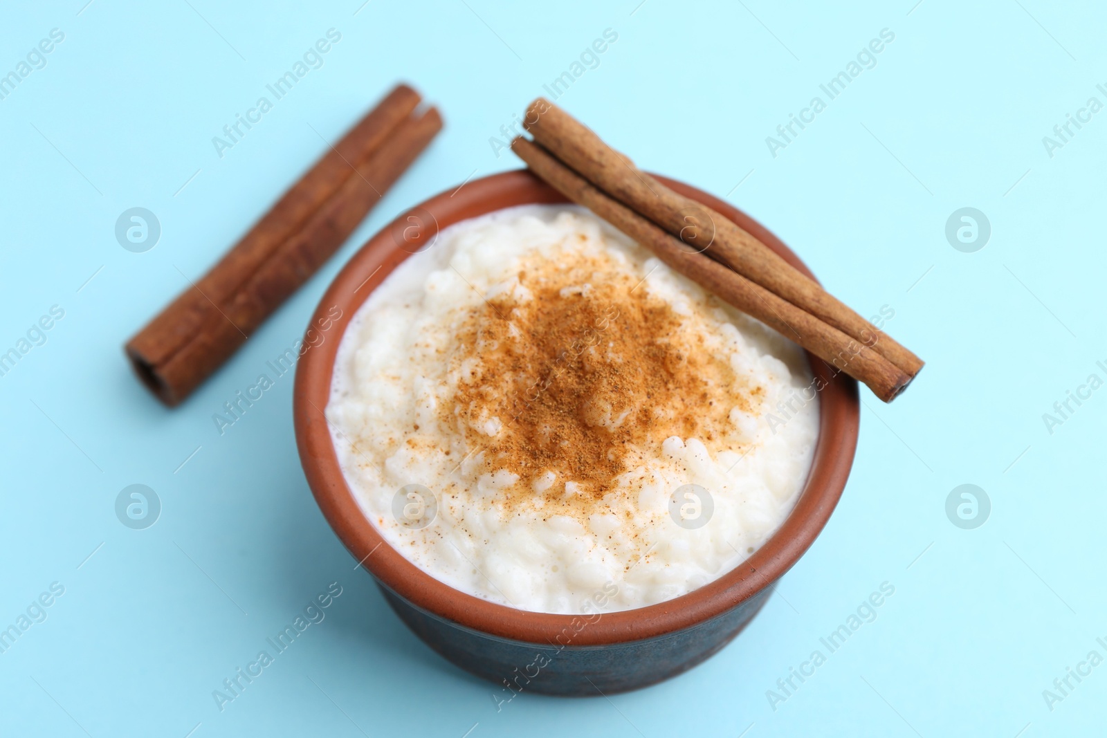 Photo of Delicious rice pudding with cinnamon sticks on light blue background, closeup