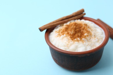 Photo of Delicious rice pudding with cinnamon on light blue background, closeup. Space for text