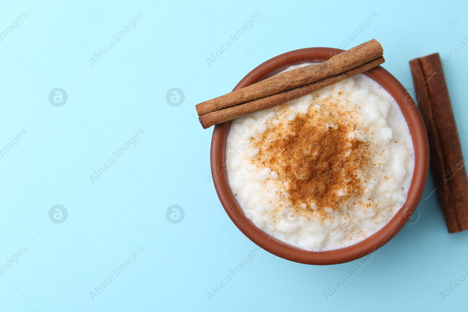 Photo of Delicious rice pudding with cinnamon sticks on light blue background, top view. Space for text