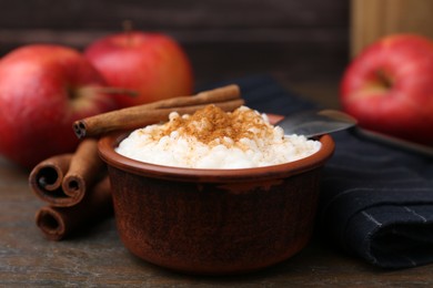 Photo of Delicious rice pudding with cinnamon sticks and apples on wooden table, closeup