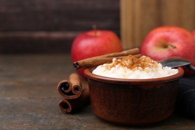 Photo of Delicious rice pudding with cinnamon sticks and apples on wooden table, closeup. Space for text