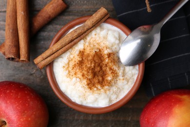 Photo of Delicious rice pudding with cinnamon sticks and apples on wooden table, flat lay