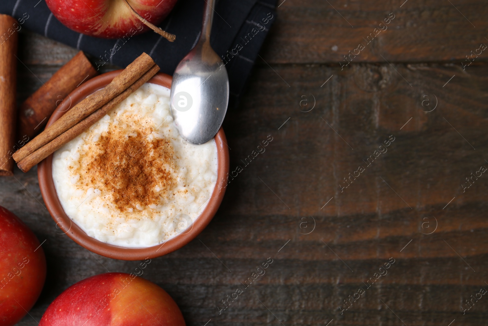 Photo of Delicious rice pudding with cinnamon and apples on wooden table, flat lay. Space for text