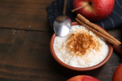 Photo of Delicious rice pudding with cinnamon and apples on wooden table, closeup. Space for text