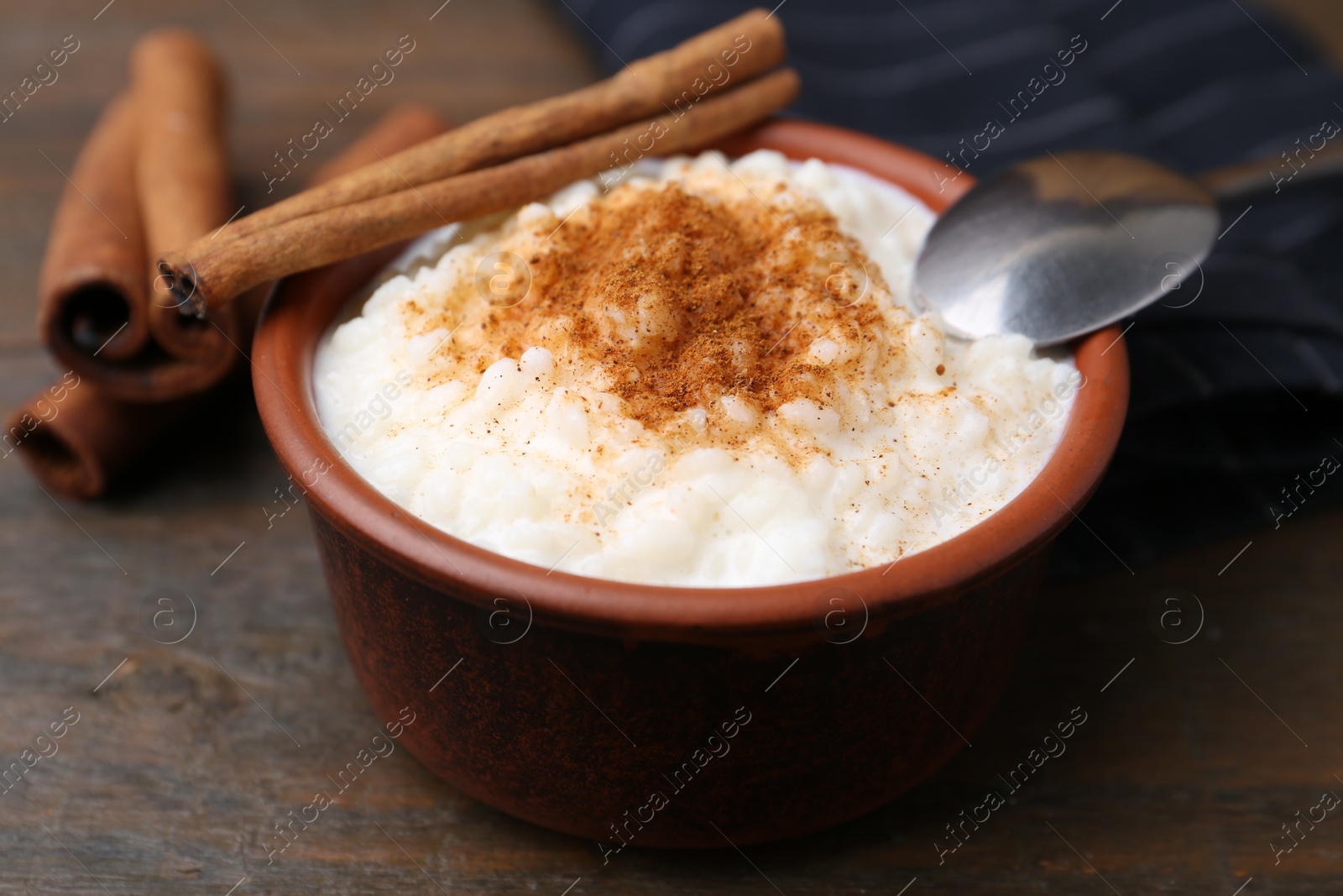 Photo of Delicious rice pudding with cinnamon sticks on wooden table, closeup