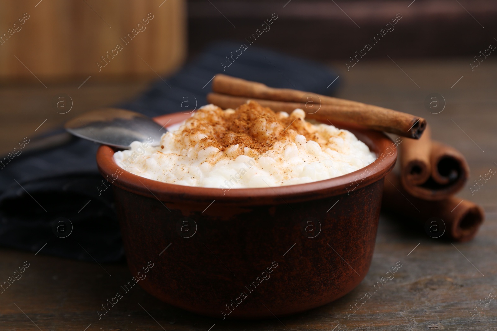 Photo of Delicious rice pudding with cinnamon sticks on wooden table, closeup