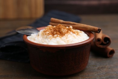 Photo of Delicious rice pudding with cinnamon sticks on wooden table, closeup