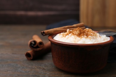 Photo of Delicious rice pudding with cinnamon sticks on wooden table, closeup