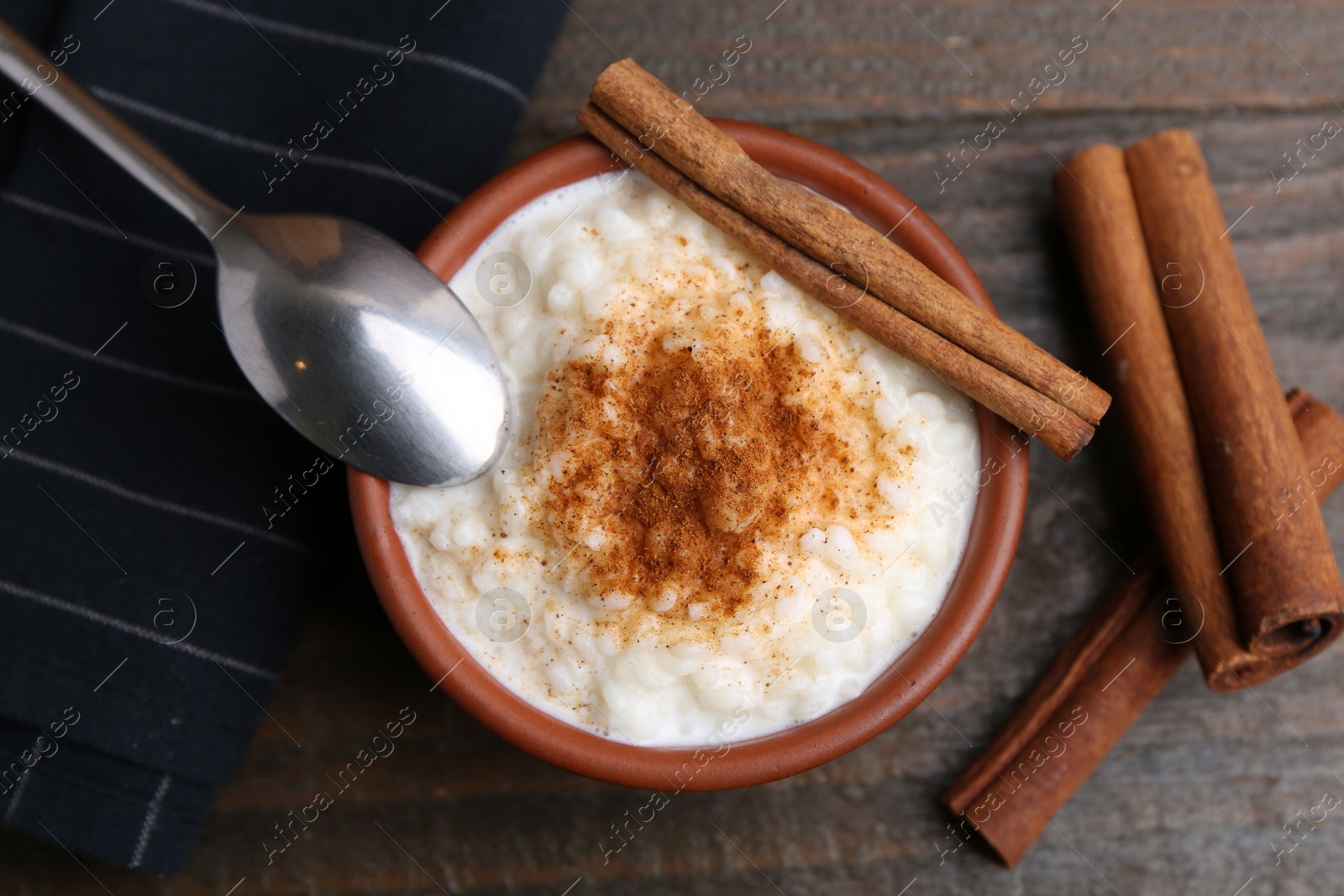 Photo of Delicious rice pudding with cinnamon sticks on wooden table, top view