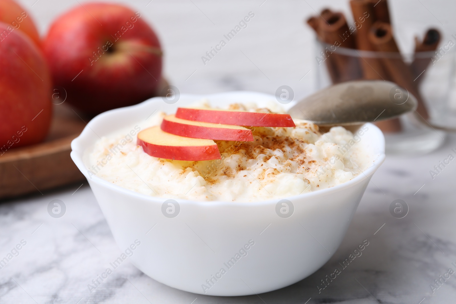 Photo of Delicious rice pudding with cinnamon and apple on white marble table, closeup