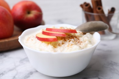 Photo of Delicious rice pudding with cinnamon and apple on white marble table, closeup