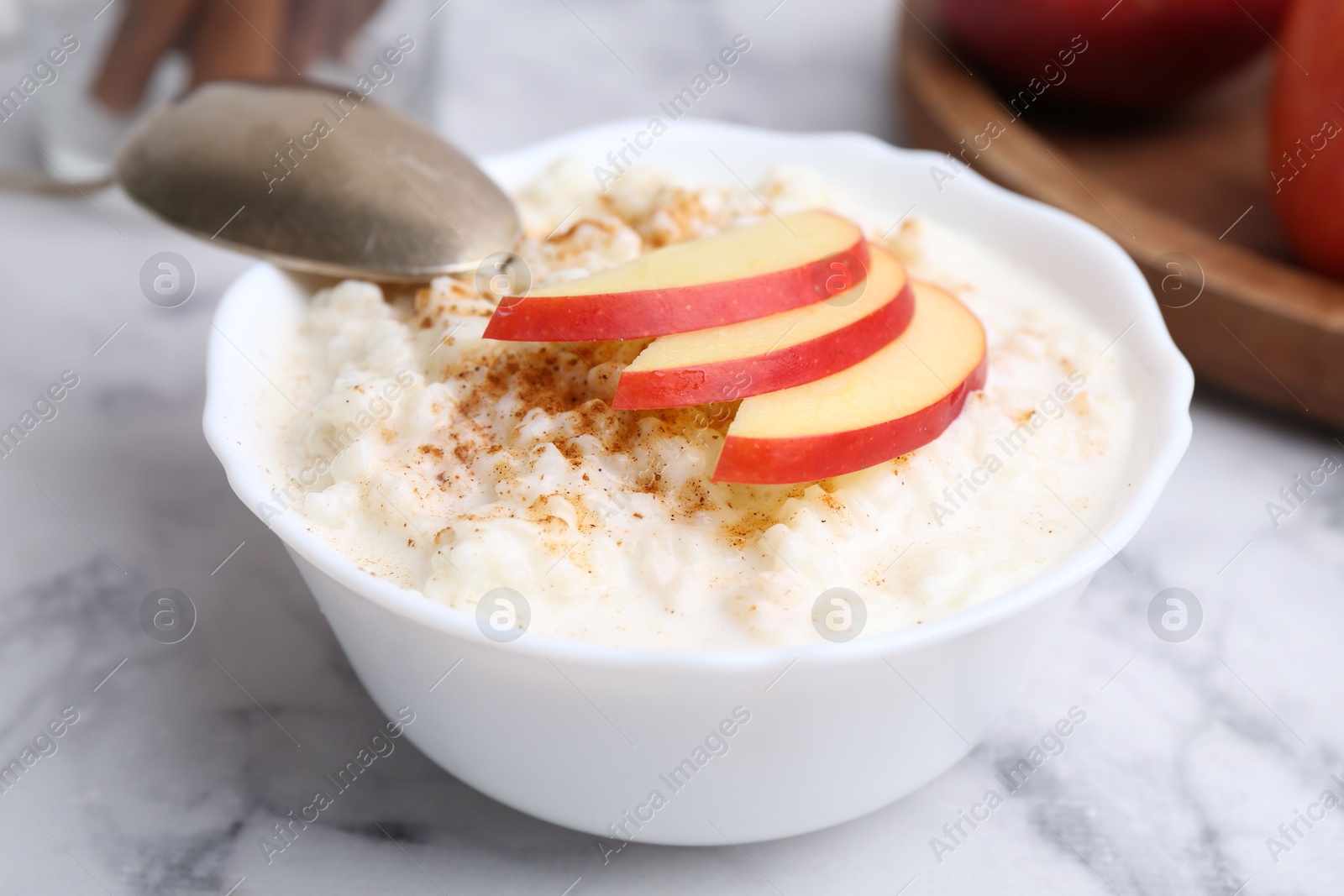 Photo of Delicious rice pudding with cinnamon and apple on white marble table, closeup