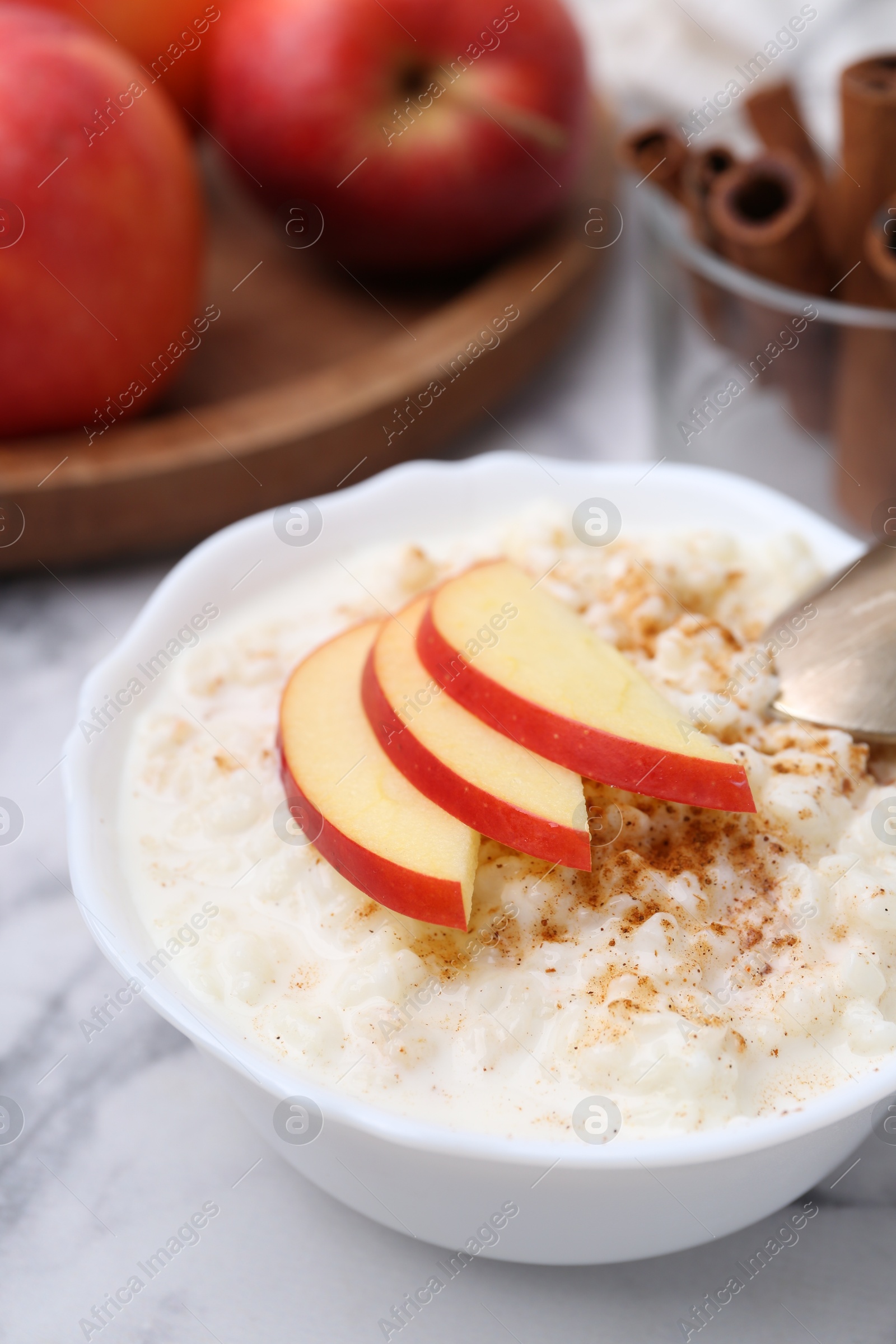 Photo of Delicious rice pudding with cinnamon and apples on white marble table, closeup