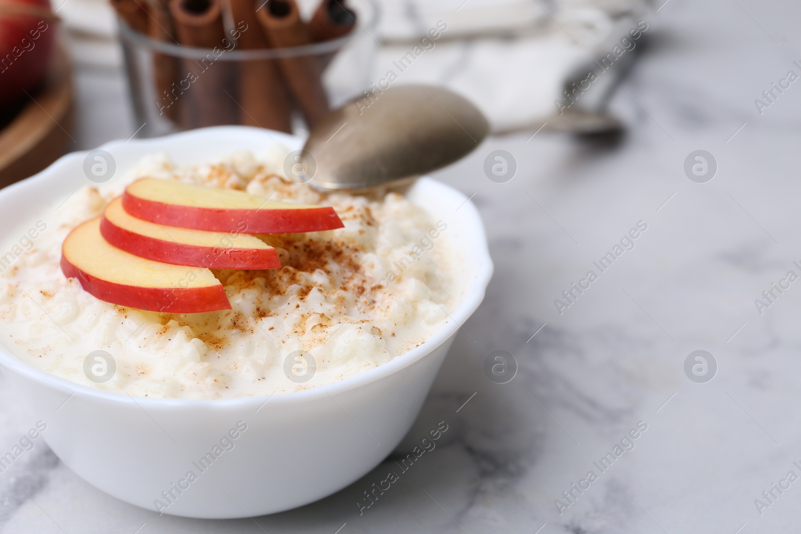 Photo of Delicious rice pudding with cinnamon and apple on white marble table, closeup. Space for text