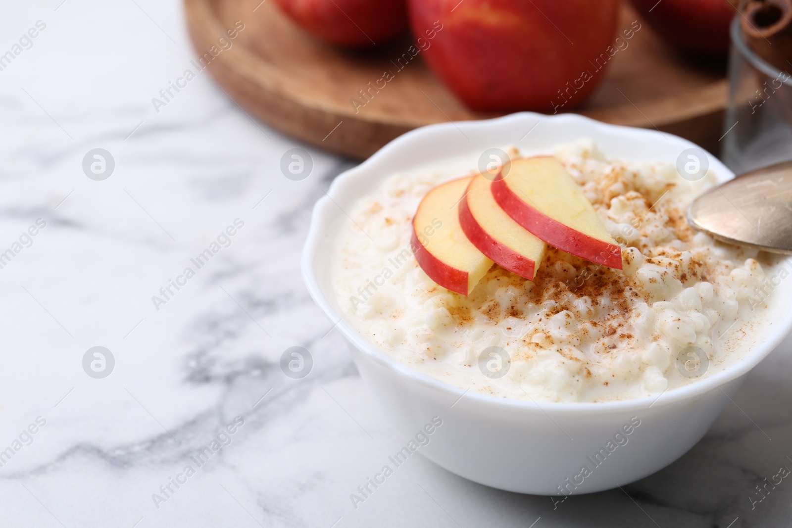 Photo of Delicious rice pudding with cinnamon and apple on white marble table, closeup. Space for text